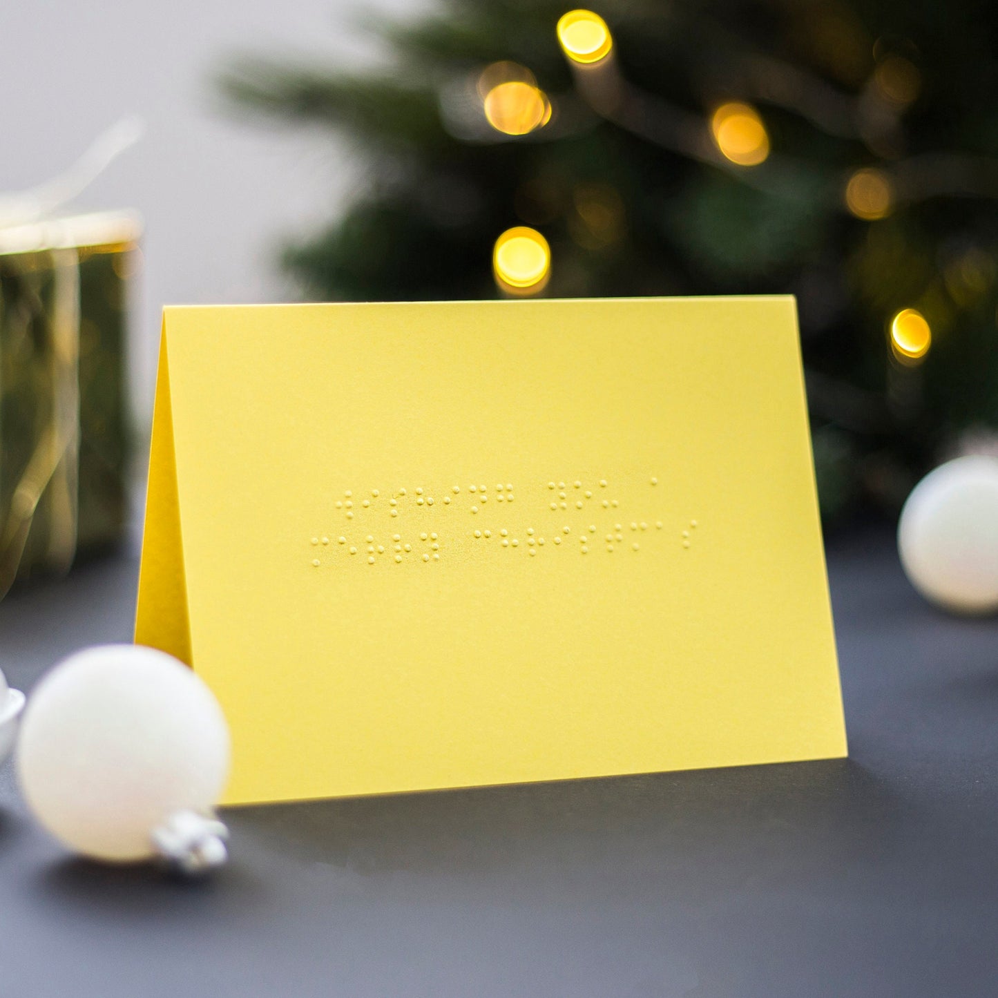 A yellow braille Christmas card saying Wishing You A Merry Christmas written in lower case UEB.