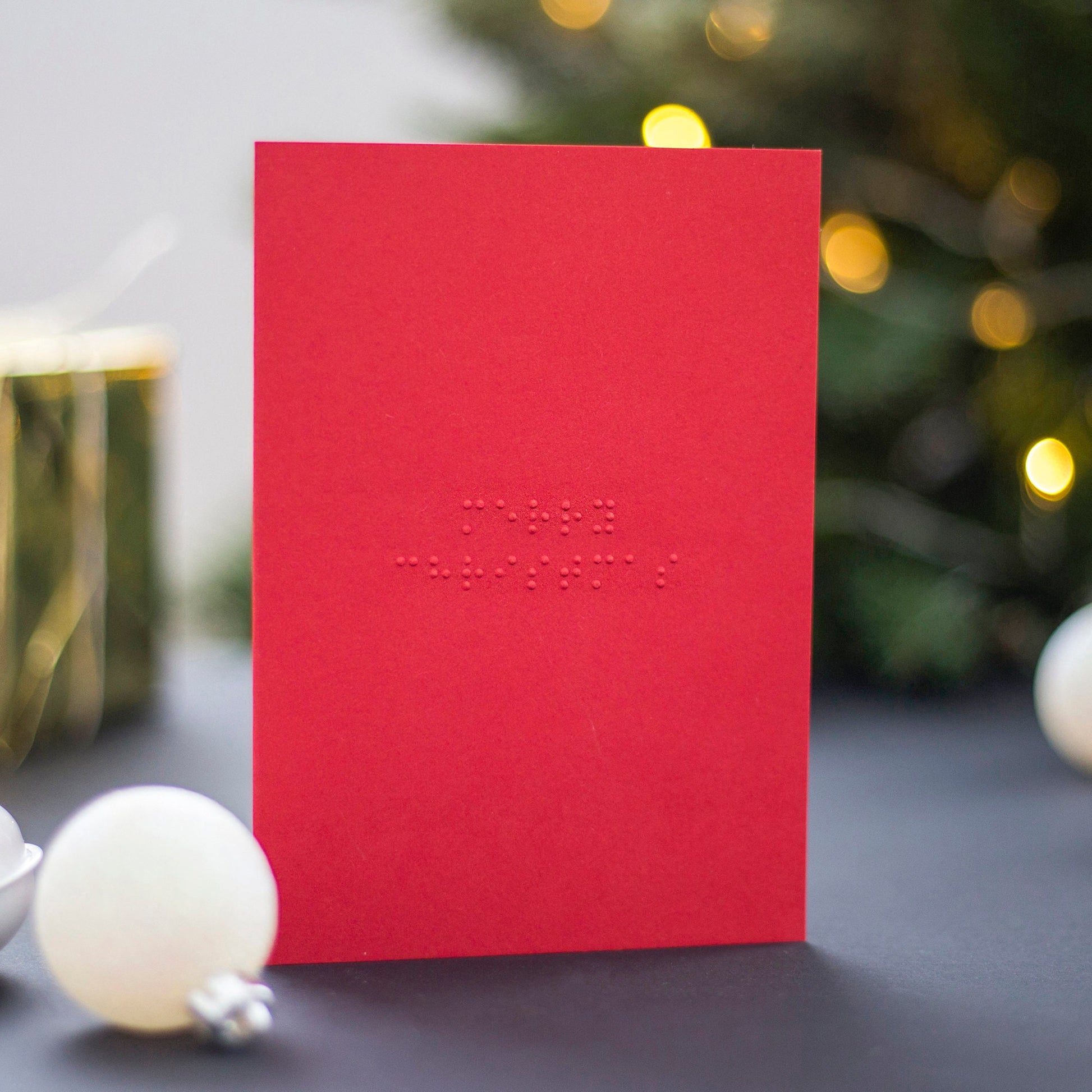 A red braille Christmas card with Merry Christmas written in lower case UEB.