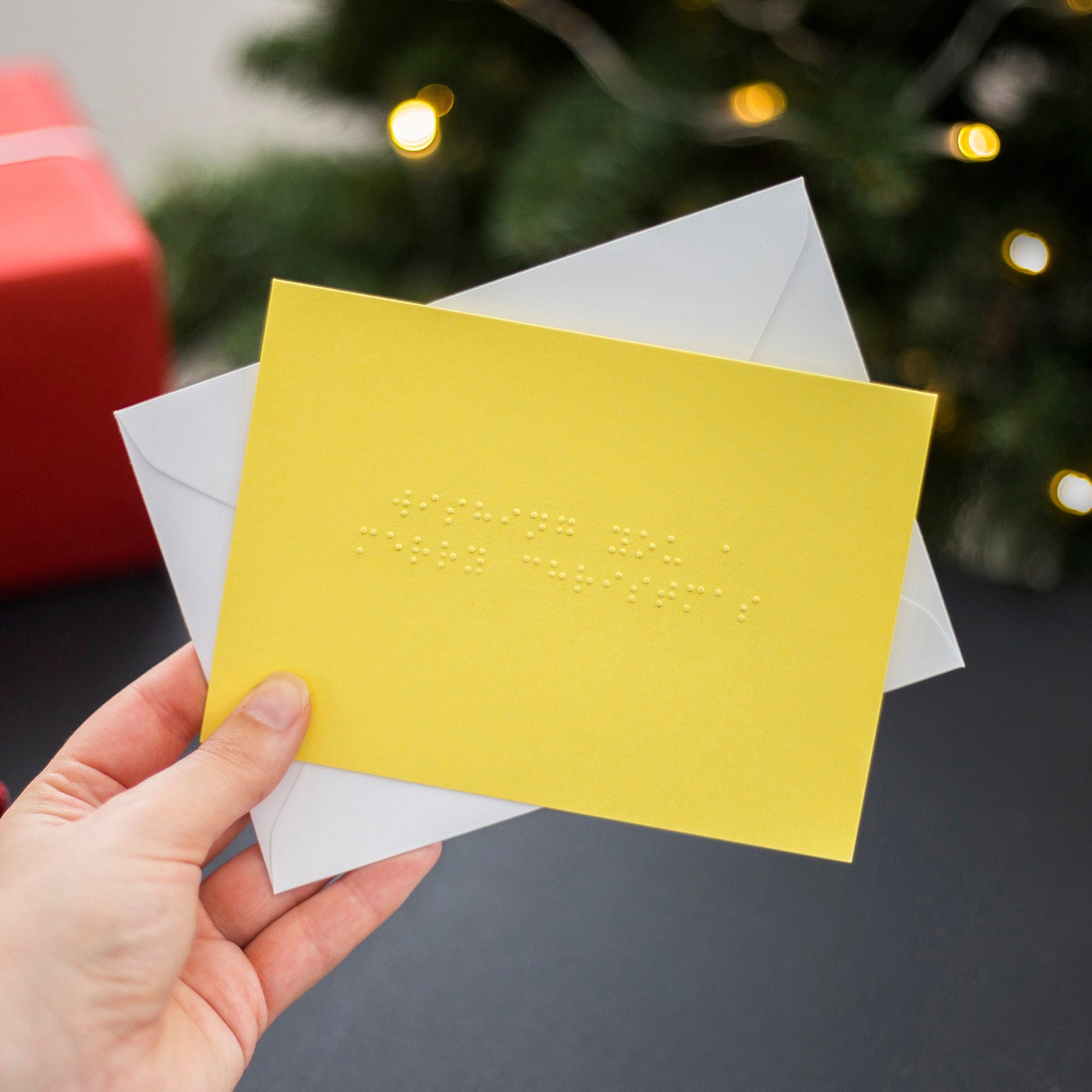 A hand holding a yellow braille Christmas card saying Wishing You A Merry Christmas written in lower case UEB.