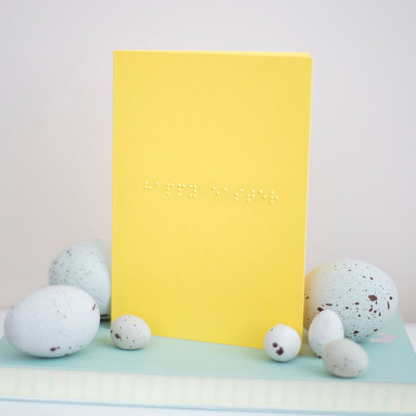 A vibrant yellow card with happy easter written in lower case braille. There are small eggs around the edges.